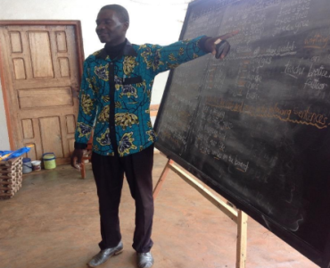 A teacher is pointing to a blackboard while teaching.