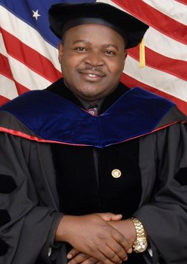 Dr.Ndiforngwa smiling with a graduation gown and american flag.